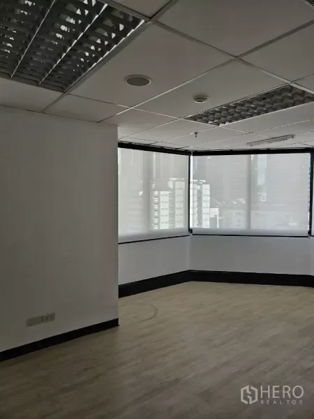 Office Space for rent in Watthana, Bangkok - Open-plan office area with large corner windows, city views through shades, and fluorescent ceiling lights.