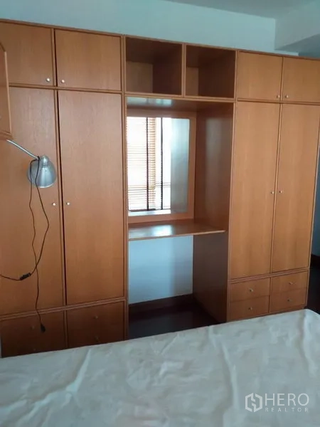 Condominium for rent in Pathum Wan, Bangkok - Bedroom featuring built-in wood wardrobes with a dressing nook and storage drawers.