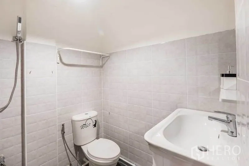 Detached House for rent in Khlong Toei, Bangkok - Compact white-tiled bathroom with shower, toilet and vanity basin.