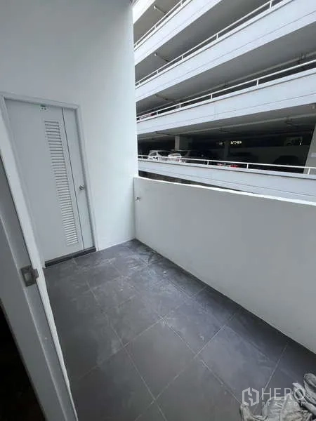 Shophouse for rent in Watthana, Bangkok - Small tiled balcony facing a multi-storey parking structure with a utility door.