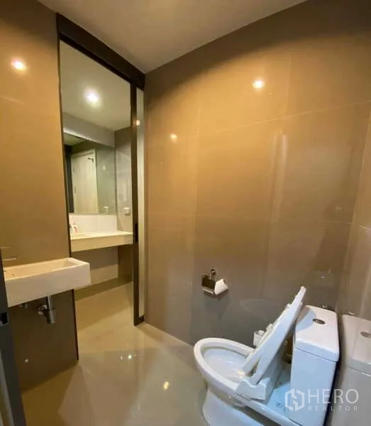 Condominium for rent or sale in Khlong Toei, Bangkok - Clean toilet room with basin, neutral tiles and view into the vanity area and shower.