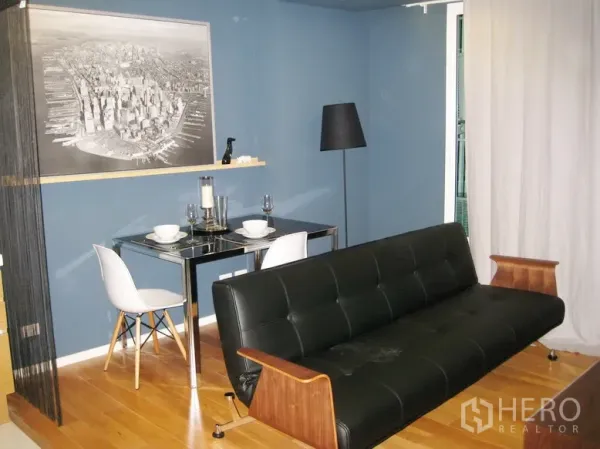 Condominium for rent or sale in Bang Rak, Bangkok - Living room with blue accent wall, black leather sofa, a dining set for two and wood floors.
