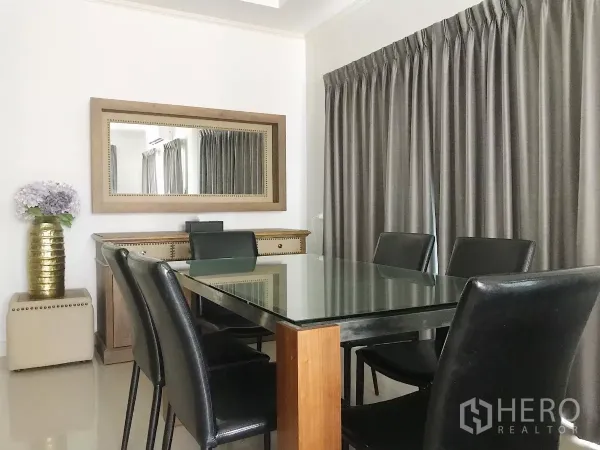 Detached House for sale in Lat Krabang, Bangkok - Dining area with glass-top table for six, large wall mirror and full-length curtains.