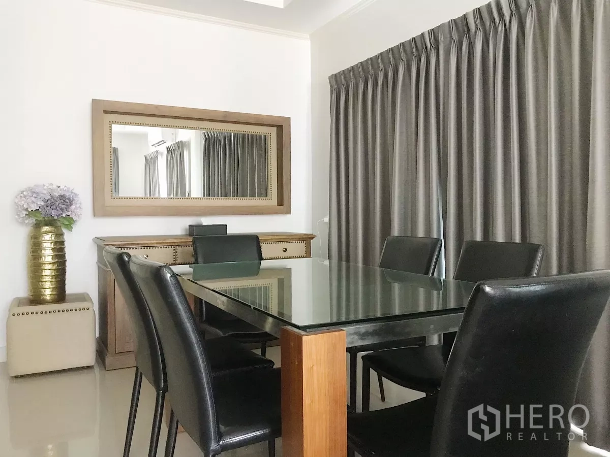 Detached House for sale in Lat Krabang, Bangkok - Dining area with glass-top table for six, large wall mirror and full-length curtains.
