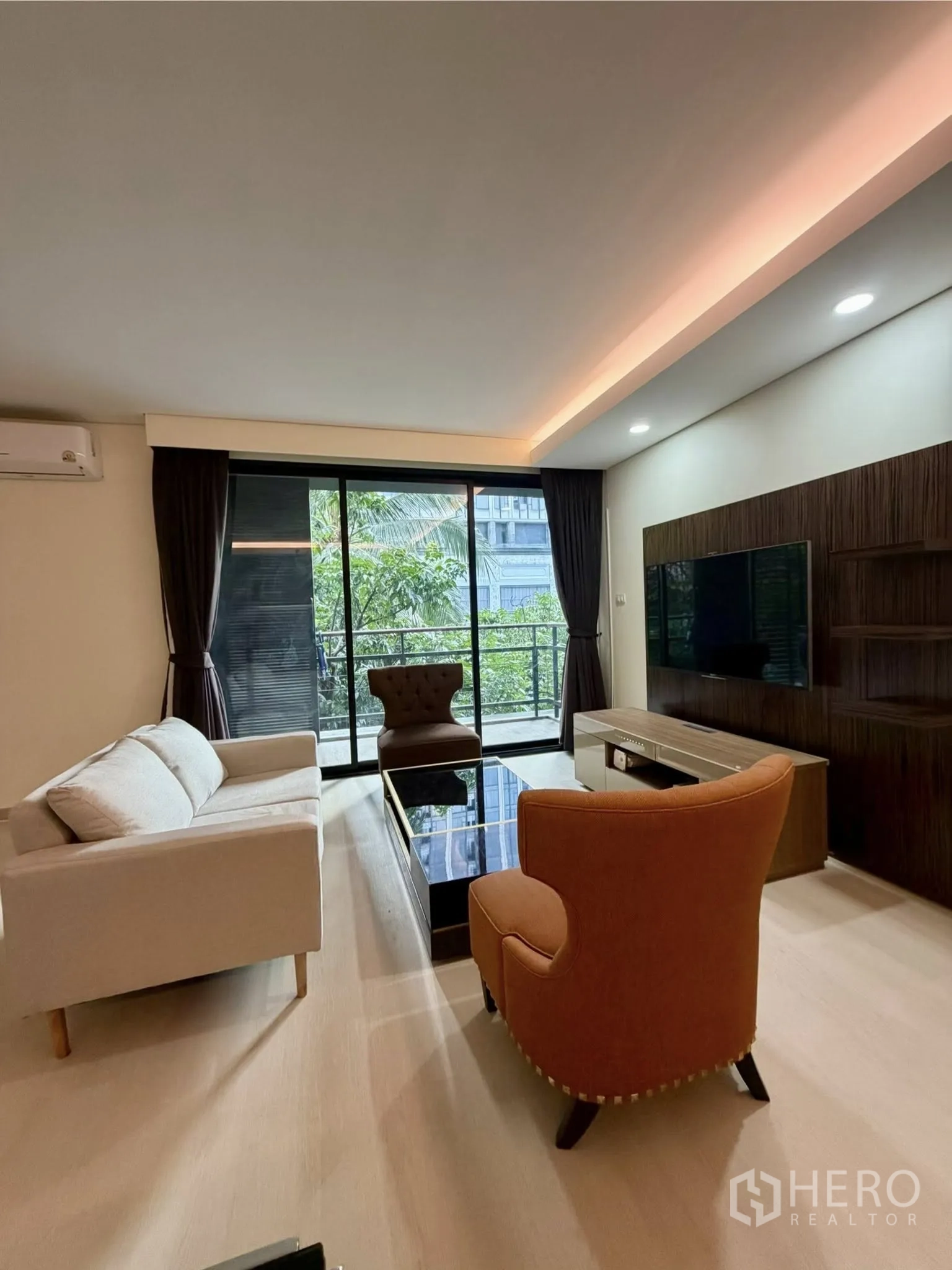 Condominium for rent in Watthana, Bangkok - Living area with sofa set, TV console, and sliding doors to a green-view balcony.