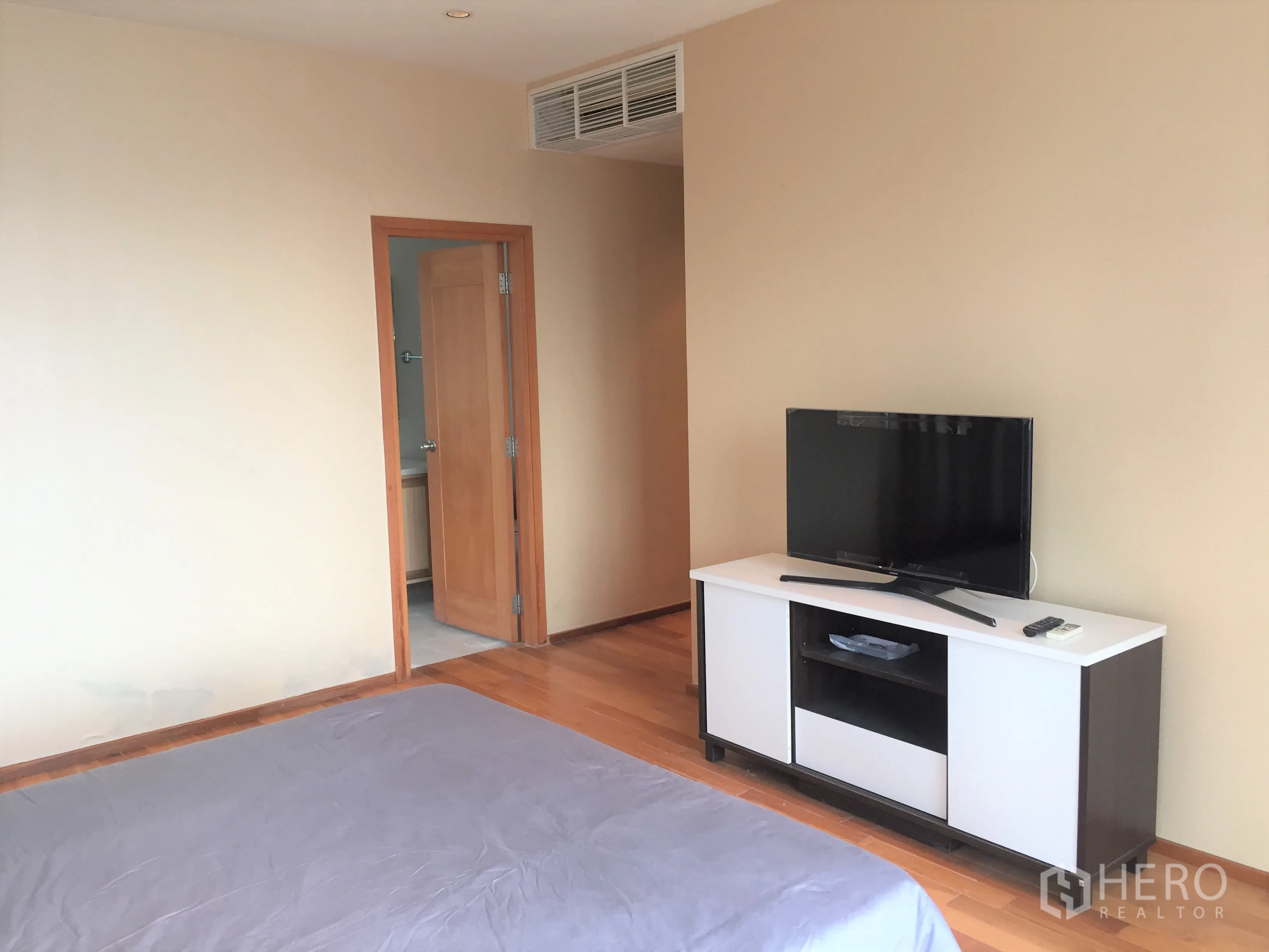 Condominium for rent or sale in Khlong Toei, Bangkok - Master bedroom with TV console, wooden floor, and door leading to an ensuite bathroom.