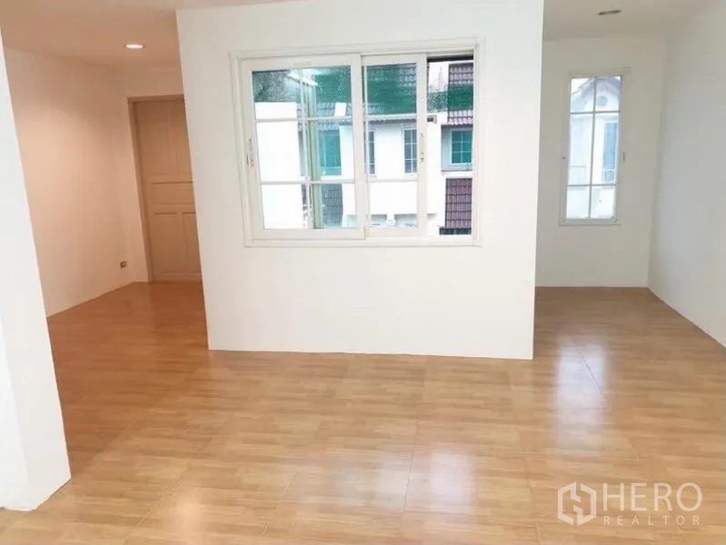 Townhouse for rent or sale in Chatuchak, Bangkok - Flexible room with light wood laminate floors and windows facing neighboring townhouses.