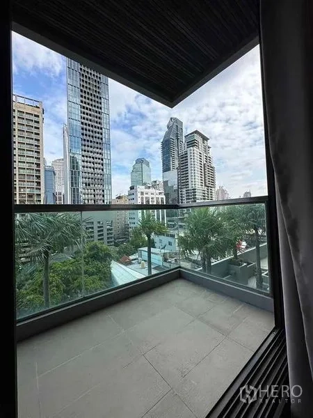公寓 出租在Khlong Toei, Bangkok - 半覆盖阳台，玻璃栏杆，眺望曼谷天际线与棕榈树。