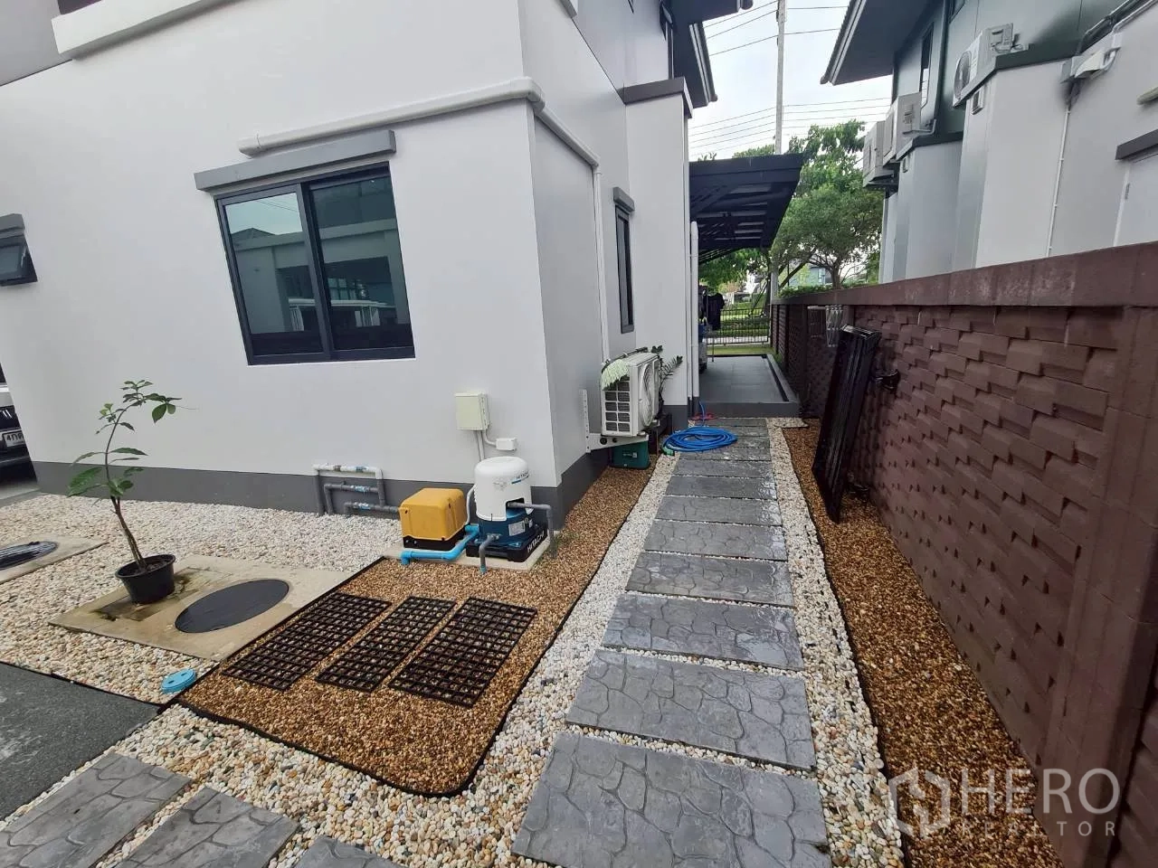 Detached House for rent or sale in Lam Luk Ka, Pathum Thani - Side yard featuring a stone walkway, pebbled landscaping and outdoor utility units.
