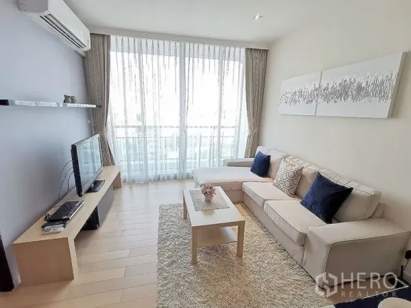คอนโด ให้เช่าในWatthana, Bangkok - ห้องนั่งเล่นสว่าง โซฟา L‑shape ชั้นวางทีวี หน้าต่างเต็มบาน และพื้นไม้โทนอ่อน