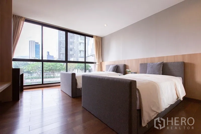 Condominium for sale in Sathon, Bangkok - Twin bedroom with two single beds and skyline view through full-height windows.