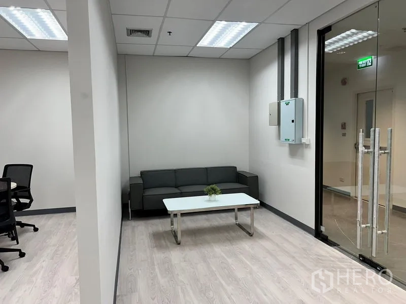 Office Space for rent in Sathon, Bangkok - Reception lounge by the glass entrance with gray sofa, white table and ceiling lighting.