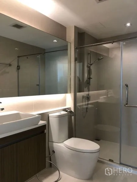 Condominium for sale in Khlong Toei, Bangkok - Second bathroom with glass‑enclosed shower, toilet and illuminated mirror.