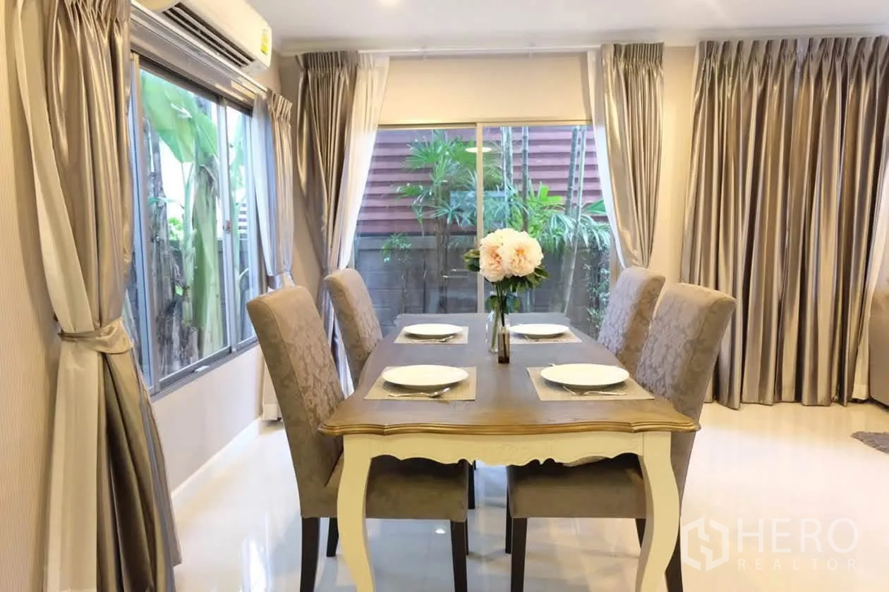 半独立式住宅 for rent or sale in Suan Luang, Bangkok - 餐区摆放四把软包椅与木桌，旁有窗户与通向花园的推拉门。