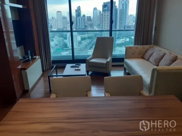 Condominium for rent or sale in Khlong Toei, Bangkok - Living room with floor-to-ceiling windows and Bangkok skyline view, wood floors, sofa and armchair.