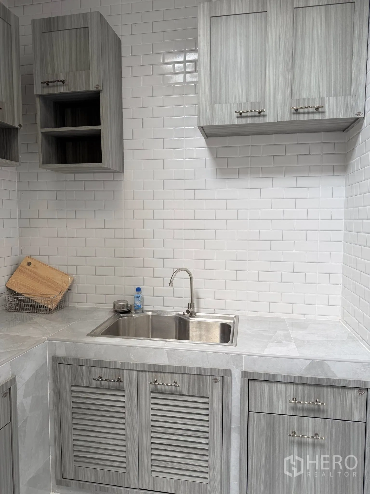 Townhouse for rent or sale in Yan Nawa, Bangkok - Kitchen sink and overhead cabinets against white tiled wall.