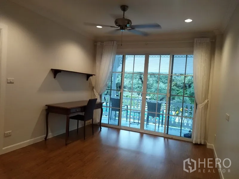 Townhouse for rent in Mueang Samut Prakan, Samut Prakan - Flexible room with desk, ceiling fan, and balcony access through wide glass doors.