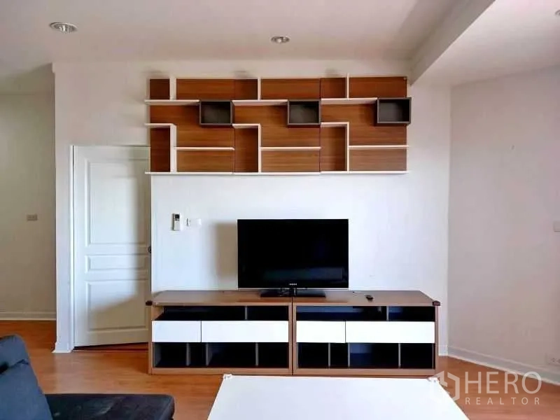 Condominium for rent in Khlong Toei, Bangkok - TV wall with modern built-in shelves and a low media console in a bright living room.