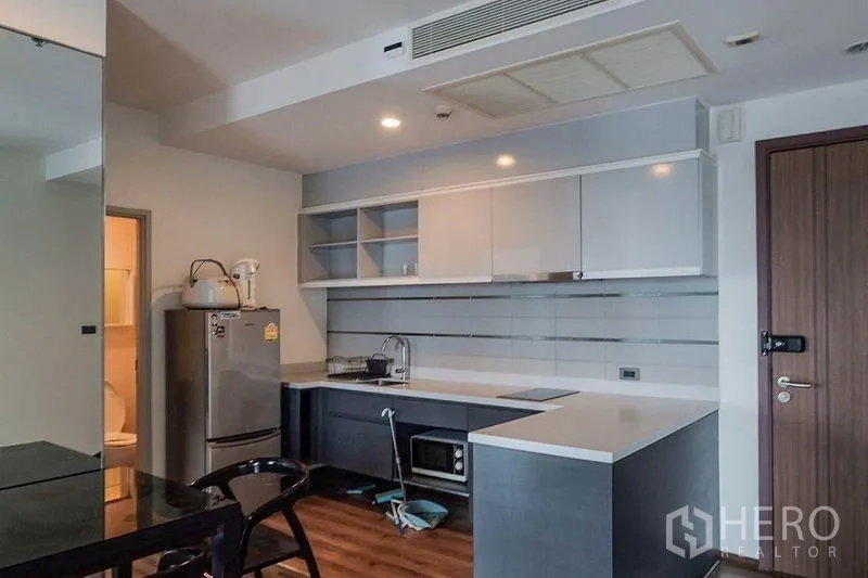 Condominium for rent in Khlong Toei, Bangkok - Open-plan kitchen with grey cabinets, white countertops, refrigerator and microwave.