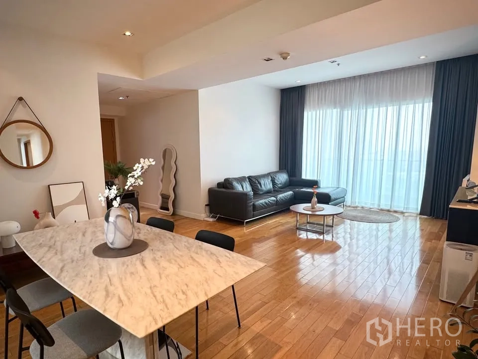 Condominium for rent or sale in Khlong Toei, Bangkok - Living and dining area with a marble-top table and black leather sofa beside full-length curtains.