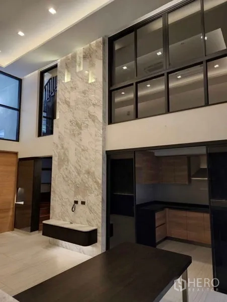 Townhouse for sale in Yan Nawa, Bangkok - Living area with soaring ceiling, marble feature wall and glass partition to the kitchen.