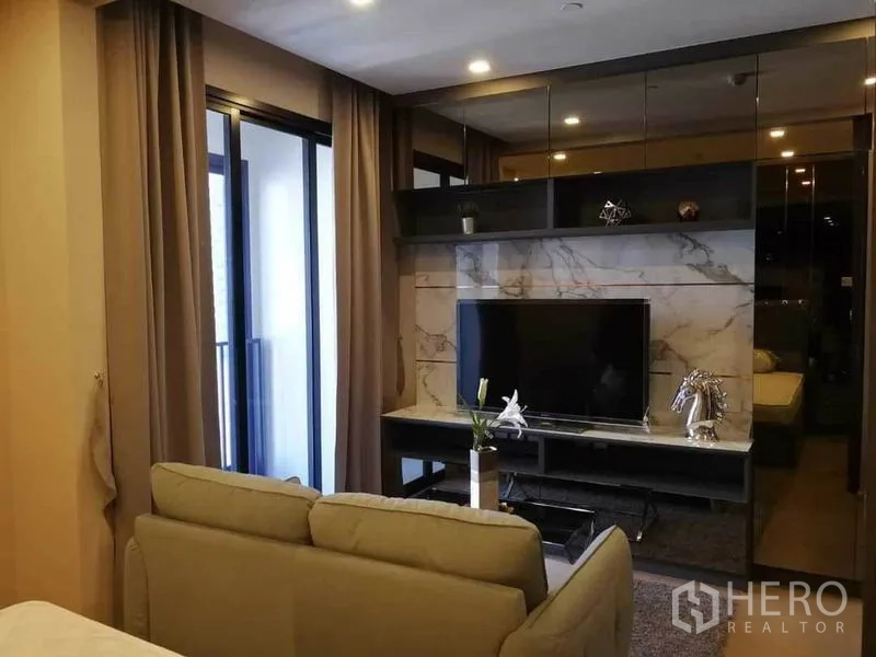 Condominium for rent in Watthana, Bangkok - Modern media wall with marble-look panel and TV opposite a sofa, beside balcony doors.