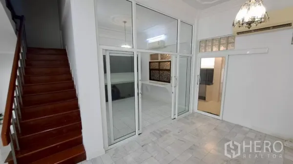 联排别墅 出租在Watthana, Bangkok - 采光良好的起居空间，推拉玻璃门与光亮木楼梯。