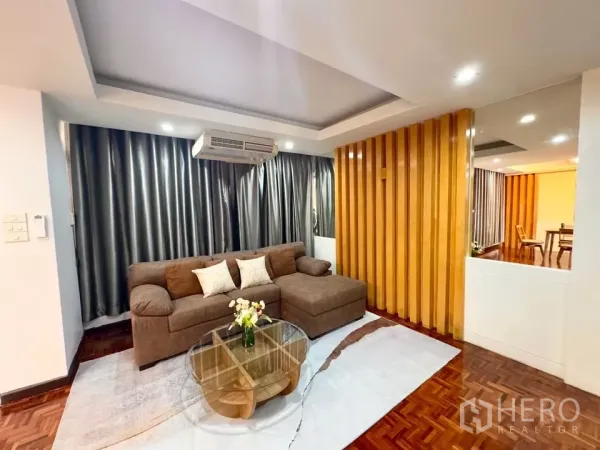 คอนโด ให้เช่าในHuai Khwang, Bangkok - ห้องนั่งเล่นกว้าง โซฟา L สีน้ำตาล ฉากกั้นไม้ เพดานหลุม และโต๊ะกระจก