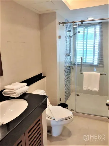 公寓 出租在Bang Rak, Bangkok - 现代浴室，玻璃淋浴间、台盆柜、马桶与采光窗。