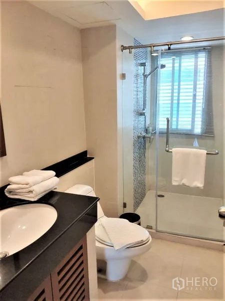 公寓 出租在Bang Rak, Bangkok - 现代浴室，玻璃淋浴间、台盆柜、马桶与采光窗。