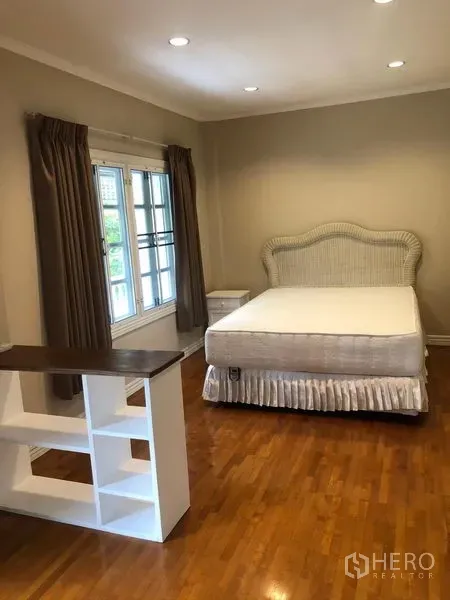 Townhouse for rent in Mueang Samut Prakan, Samut Prakan - Cozy bedroom with bed, bedside table, large windows with curtains, and warm wood floors under recessed lighting.