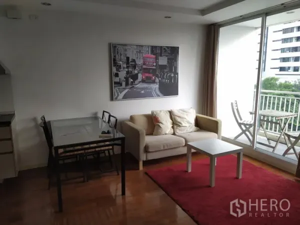 Condominium for sale in Khlong Toei, Bangkok - Bright living area with sofa, glass dining table and sliding doors to a balcony with seating.