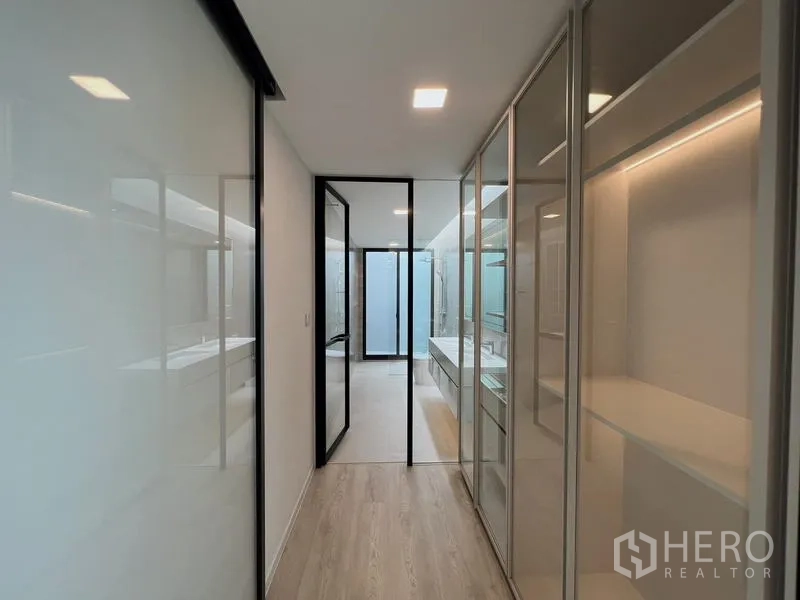 Detached House for rent or sale in Saphan Sung, Bangkok - Walk-through closet corridor with glass wardrobes connecting to the ensuite bathroom.