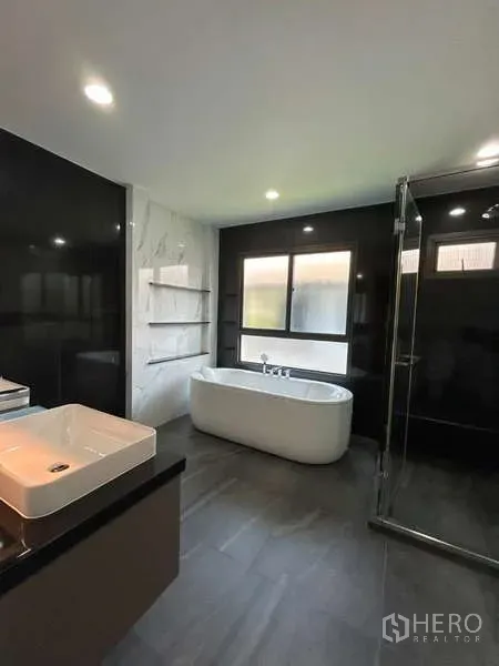 Detached House for rent in Bang Kapi, Bangkok - Modern bathroom with freestanding bathtub, glass shower, large window and black-and-white tile walls.