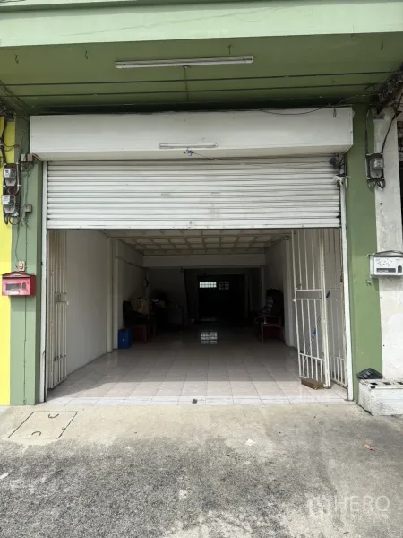 Shophouse for rent in Pak Kret, Nonthaburi - Street-level shophouse facade with white roller shutter and tiled entry.