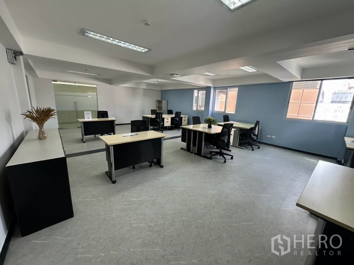 Office Space for rent in Watthana, Bangkok - Open workspace facing windows with manager desks and a long storage credenza along the wall.