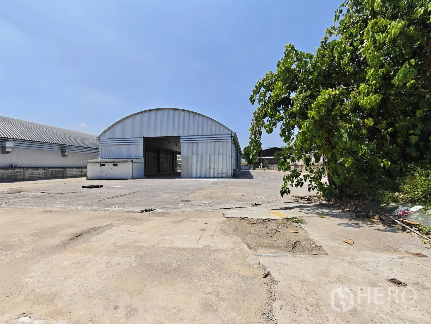 Warehouse for rent in Lak Si, Bangkok - Front view of the warehouse with sliding industrial door and broad concrete forecourt beside trees.
