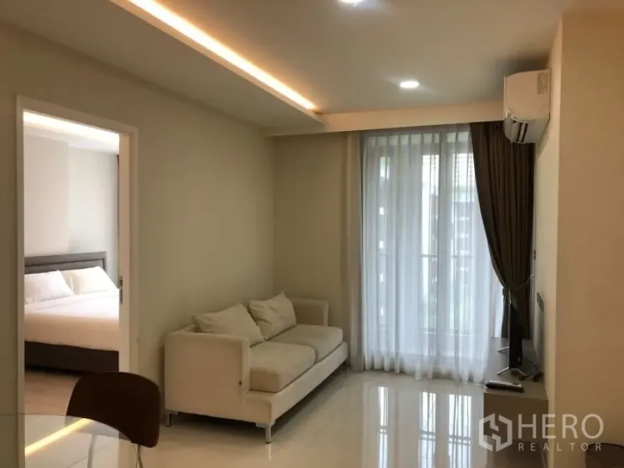 Condominium for sale in Khlong Toei, Bangkok - Open‑plan view from entry showing kitchen flowing to living area and balcony with recessed lighting.