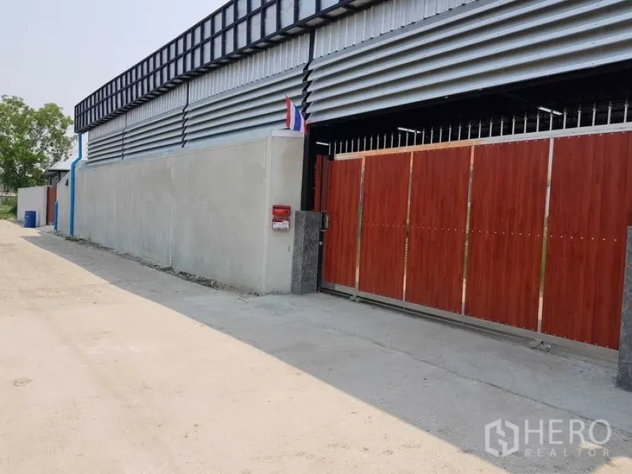 Warehouse for sale in Lam Luk Ka, Pathum Thani - Front elevation of the warehouse with wood-look sliding gate along a quiet access lane.