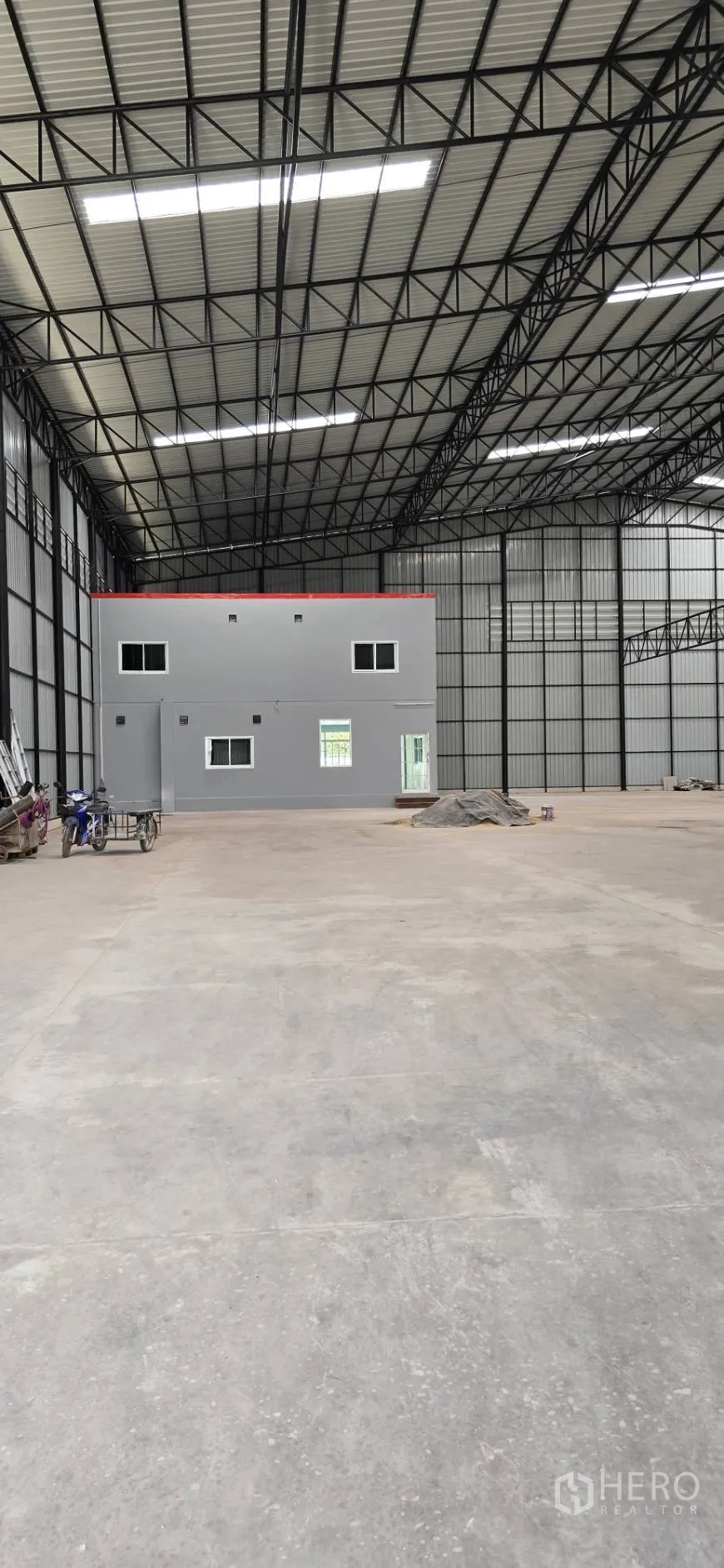โรงงาน for rent in Mueang Samut Sakhon, Samut Sakhon - ภายในโกดังพื้นที่กว้าง เพดานโครงทรัสเหล็ก พื้นคอนกรีต และออฟฟิศสองชั้นสีเทาด้านหลัง.