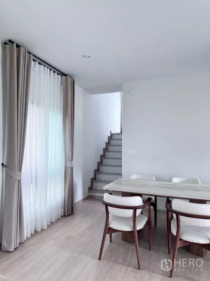 Detached House for rent in Lat Krabang, Bangkok - Dining area beside staircase and large windows with neutral curtains.