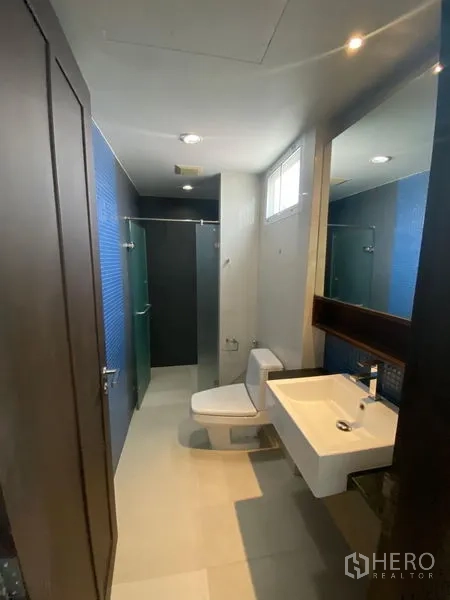 公寓 出租在Watthana, Bangkok - 浴室带蓝色点缀墙砖、玻璃淋浴间、马桶与墙面镜。