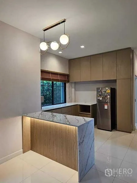 Detached House for sale in Bang Kruai, Nonthaburi - Light wood kitchen with marble island, pendant lighting, ample cabinetry and a window.