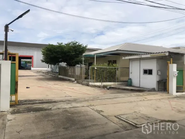 Factory for rent in Mueang Samut Prakan, Samut Prakan - Entry gate with tree-lined yard and view of metal factory warehouse