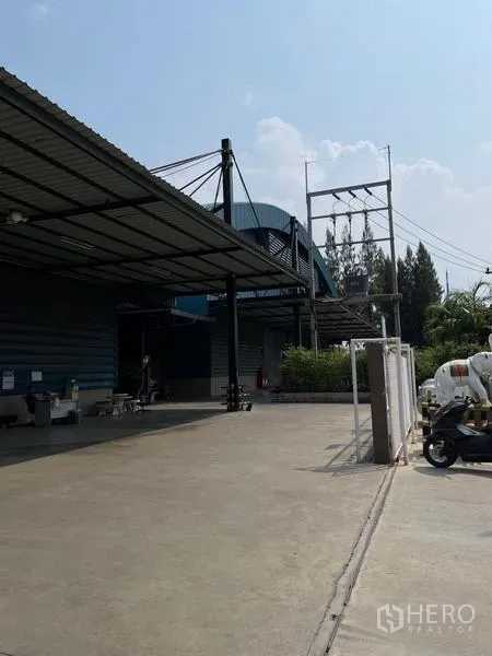 Warehouse for rent in Si Racha, Chon Buri - Side view of the warehouse with a wide concrete yard, canopy roof, and power infrastructure.