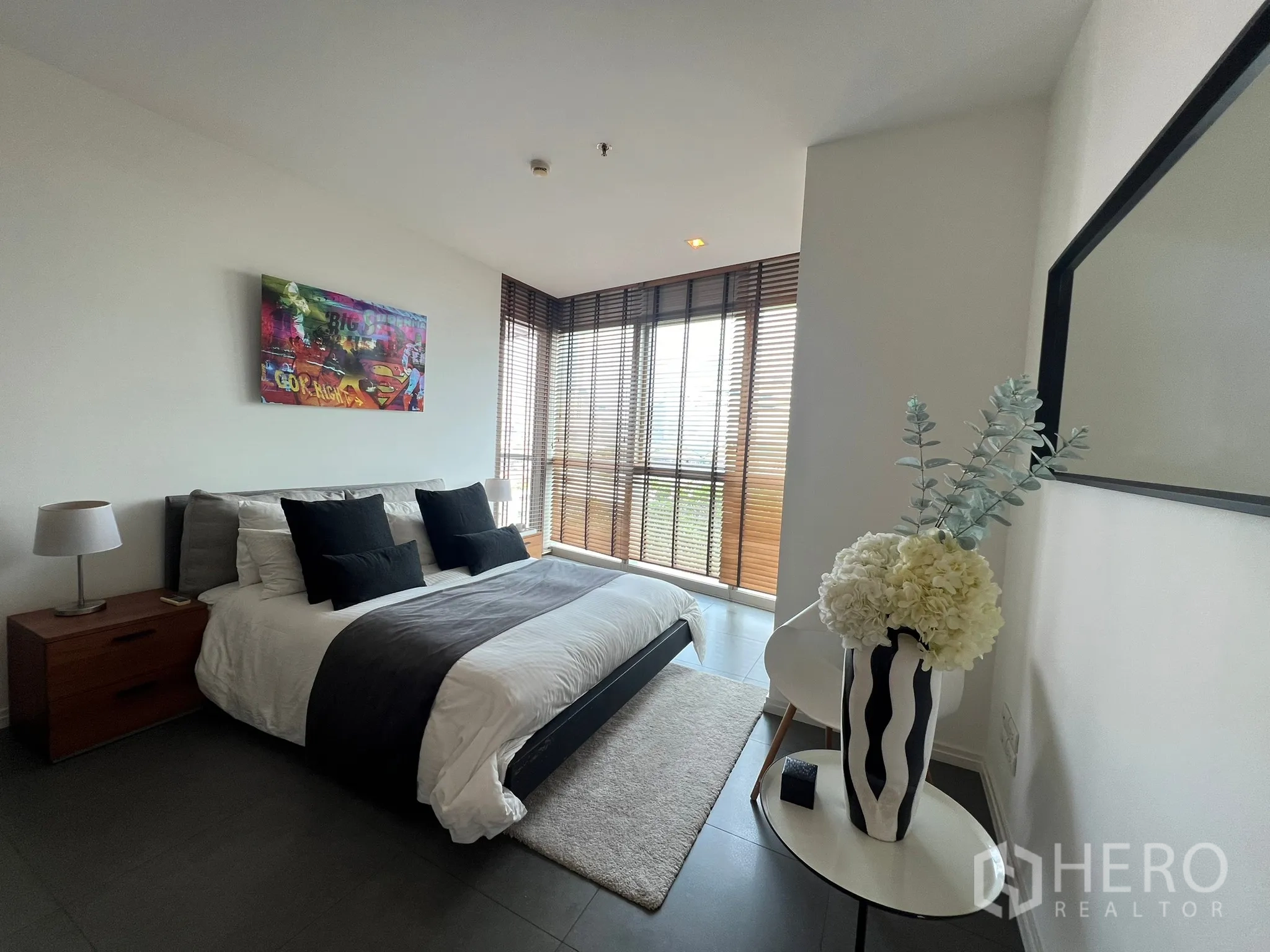 Condominium for sale in Khlong San, Bangkok - Sunlit bedroom with artwork above the bed and wraparound corner windows.