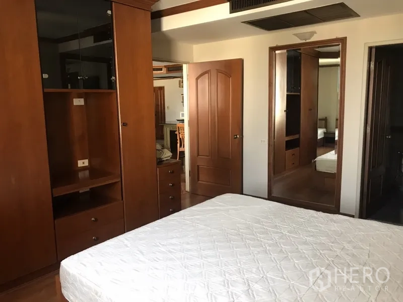 公寓 出租在Watthana, Bangkok - 主卧配双人床、木质衣柜、墙镜及通往浴室的门。