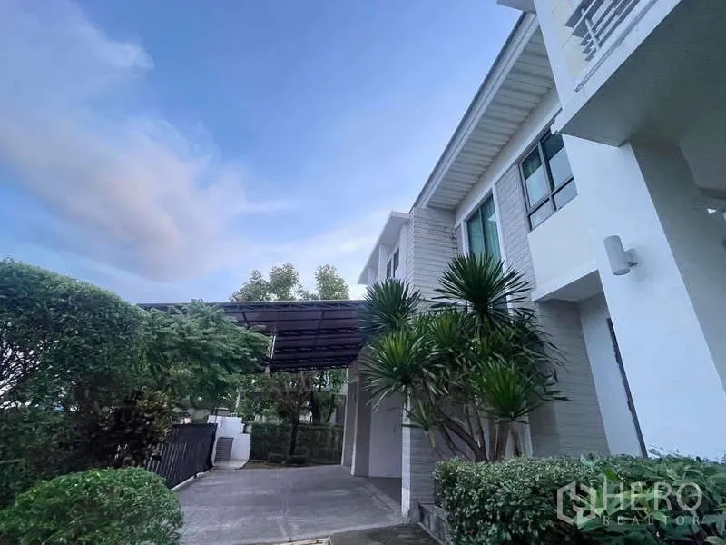 独立式住宅 出租在Mueang Nonthaburi, Nonthaburi - 前庭车道与入口雨棚，热带景观点缀其间。