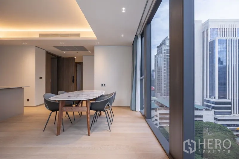 Condominium for rent in Pathum Wan, Bangkok - Dining table by floor-to-ceiling glass with skyline views of office towers.