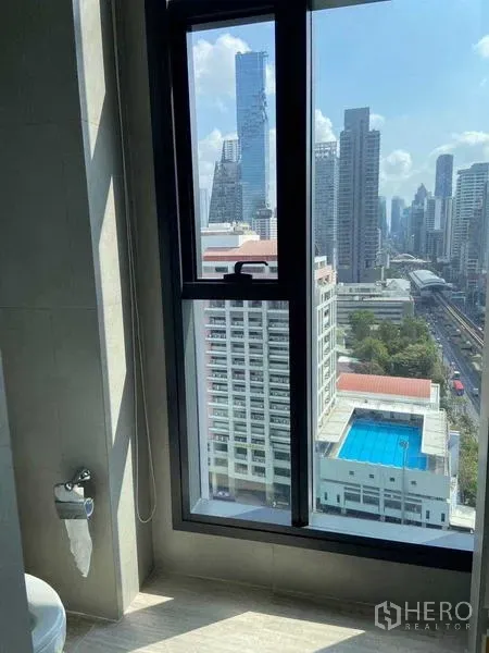 公寓 出售在Bang Rak, Bangkok - 高楼窗景俯瞰曼谷天际线、轻轨与蓝色屋顶泳池。